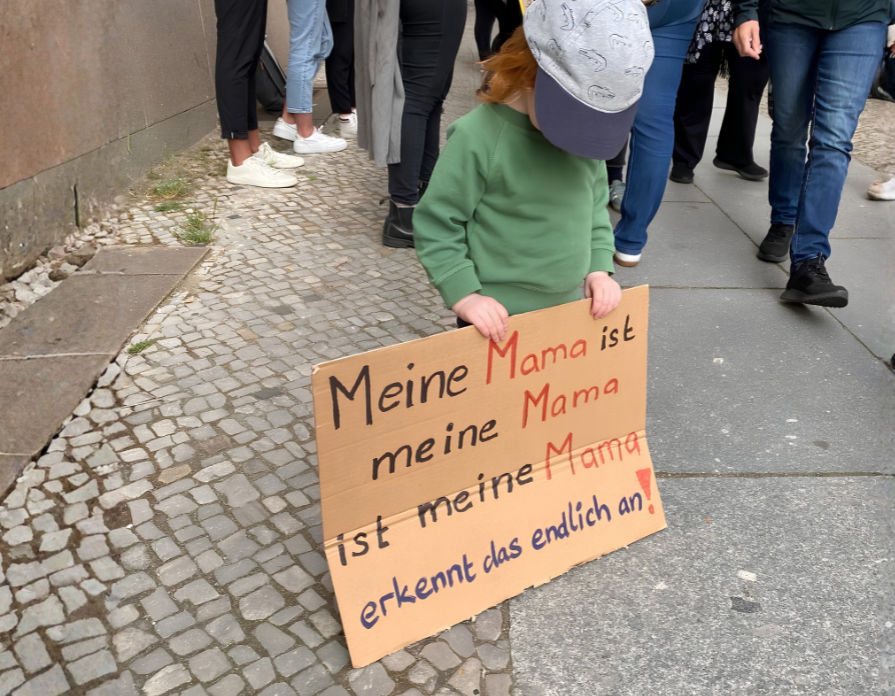 Wartende Familie Zwei Mütter sitzen mit ihrem Kleinkind auf einer Bank in einem Gebäude und warten.